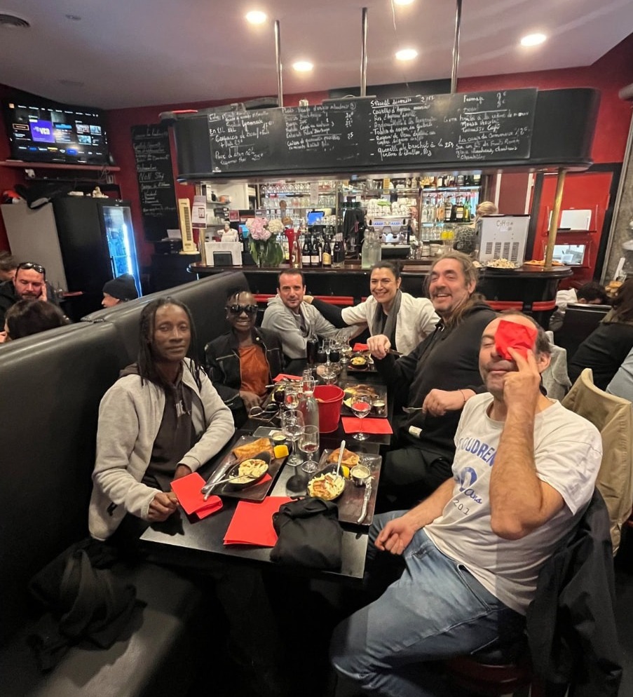 Tablée de convives installée devant le comptoir et l'ardoise des spécialités lyonnaises, l'un d'eux dissimulant son œil d'une serviette rouge