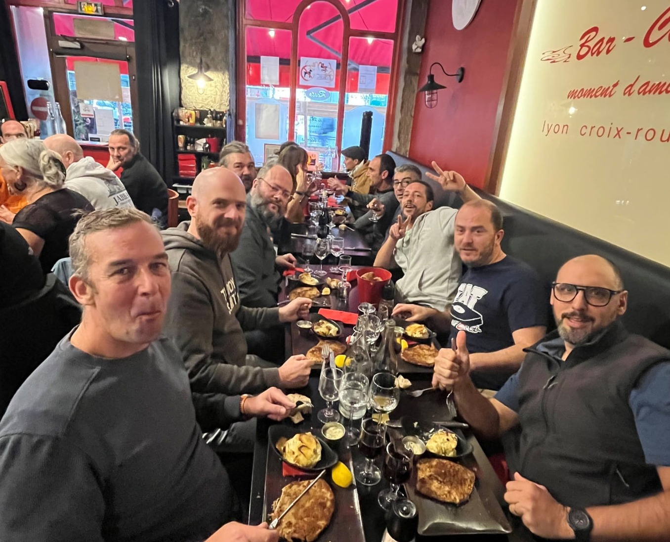 Grande tablée d'amis souriants attablés le long de la banquette, assiettes et verres de vin devant eux