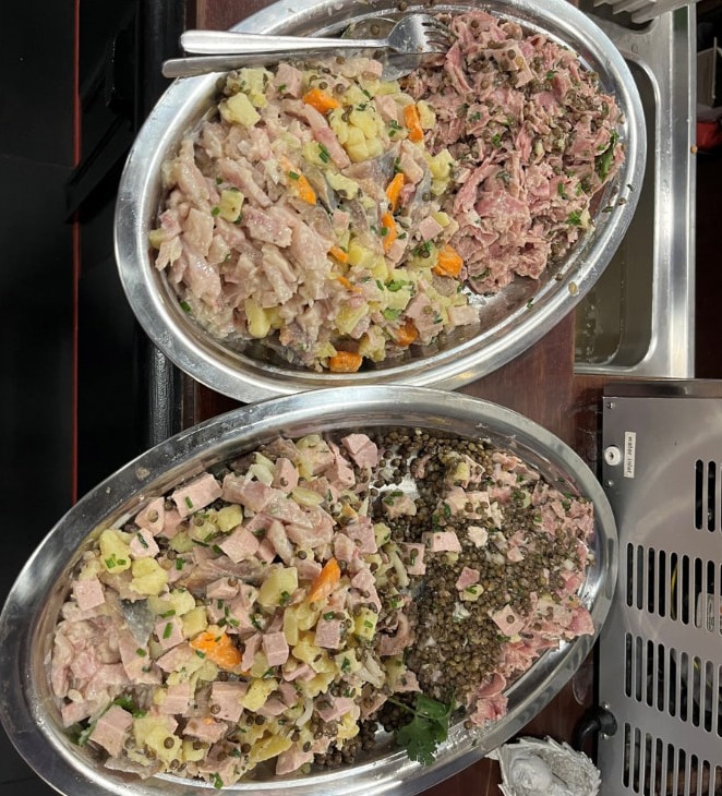 Deux grands plats ovales en inox garnis de salades lyonnaises à partager, posés sur le comptoir